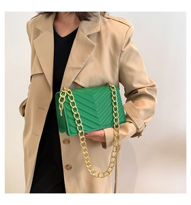 Detail of bright green quilted shoulder bag with gold chain strap on beige coat