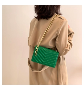 Close-up of green quilted leather shoulder bag with thick gold chain strap on a model