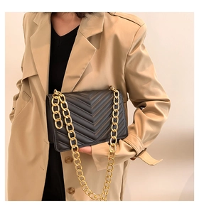 Detail of black leather crossbody bag featuring V-shaped quilting and golden chain strap