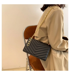 Detail of black V-quilted faux leather bag with chunky gold chain strap on model