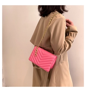 Close-up of bright pink crossbody bag featuring V-shaped quilting and gold chain strap