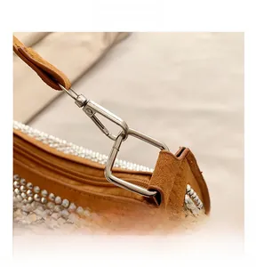 Close-up of metallic hardware hook and silver rivets on a brown suede crescent bag