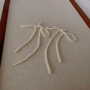 Handcrafted pearl bow tassel earrings with s925 silver needles on linen background