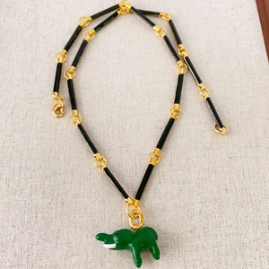 Bamboo chain necklace with green enamel elephant pendant on textured fabric background