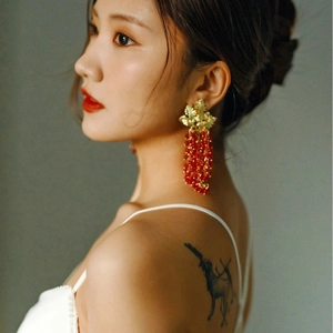 Elegant gold leaf earrings with hanging garnet red bead tassels worn by a model