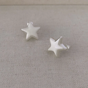 Orecchini a lobo minimalisti a stella argento opaco su tessuto beige con chiusure trasparenti