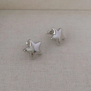 Orecchini a stella in argento lucido dal design minimalista su sfondo di tela