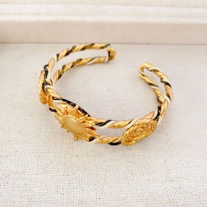Détail d'un bracelet ouvert doré vintage avec corde torsadée et relief rose