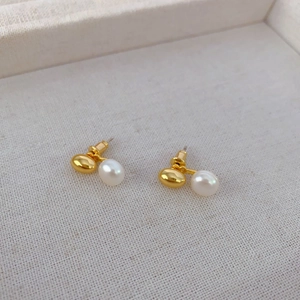 Gros plan de boucles d'oreilles perles dorées polies sur un tissu texturé doux