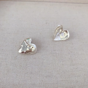 Textured silver heart earrings with hammered surface on minimalist linen background