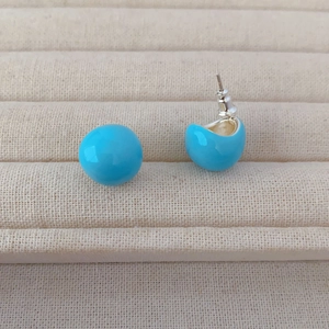 Macro shot of sky blue enamel stud earrings on a textured display with silver pins