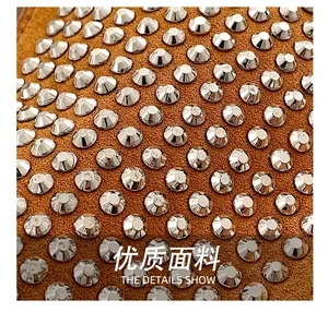 Macro detail of silver rhinestones and rivets on camel brown suede crescent handbag fabric