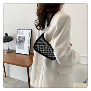 Detail of black underarm bag with silver studs worn by a model in a beige blazer