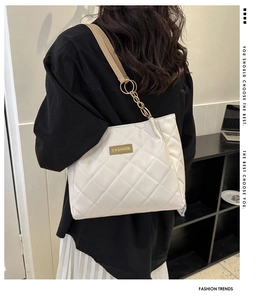 Detail of white quilted tote bag with golden chain strap and fashion label detail
