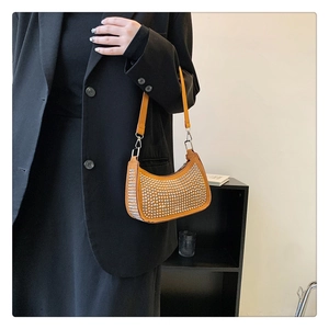 Close-up of vibrant orange crescent handbag with silver studs on black blazer outfit