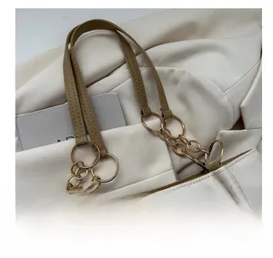 Detail of white quilted tote bag with brown leather handles and gold metal chain rings