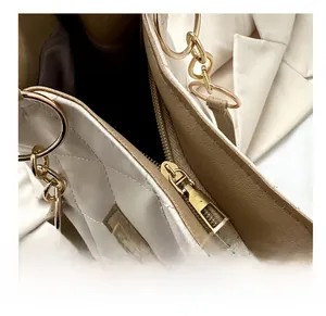 Detail of a gold-tone zipper on a quilted cream tote bag with dark brown lining