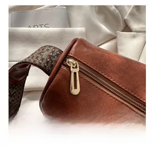 Macro detail of golden metal zipper and vintage geometric woven strap on a brown cylinder bag