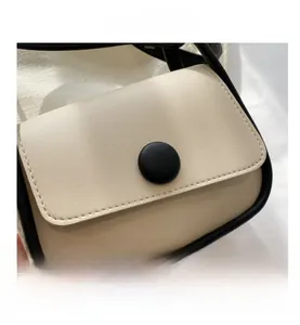 Close-up of cream crossbody bag with black contrast piping and round buckle detail