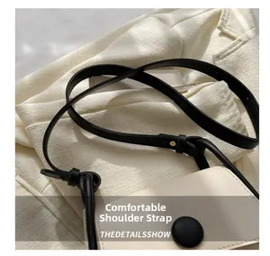 Detail of contrast stitch mini crossbody bag featuring a round decorative buckle and strap