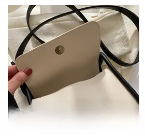 Detail view of a cream leather crossbody bag featuring a gold magnetic ring clasp
