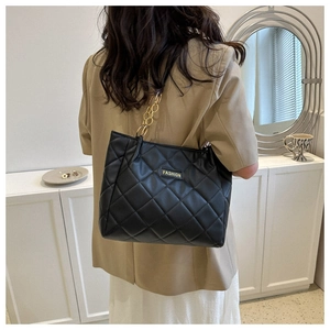 Close-up of the quilted leather texture and golden metal chain strap on a black tote bag