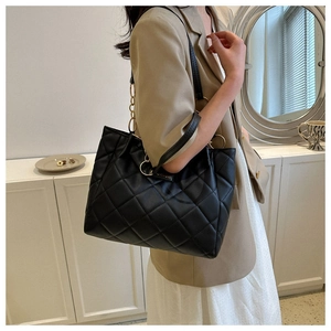 Detail of black quilted leather tote bag with large diamond stitching and gold chain strap