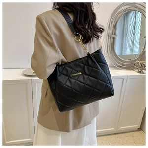 Detail of black quilted tote bag with golden chain strap and Fashion label on person