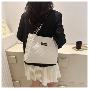 Detail of white quilted tote bag featuring golden chain strap and a fashion logo label