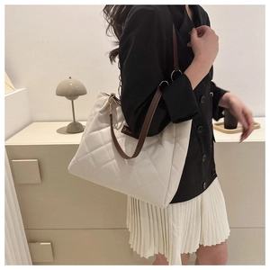 Detail of white quilted tote bag featuring a leather strap and golden chain buckle