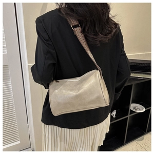 Detail of beige cylinder bag with a geometric pattern wide strap worn by a model