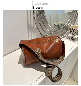 Dettaglio borsa a cilindro marrone in pelle con tracolla intrecciata e zip dorata