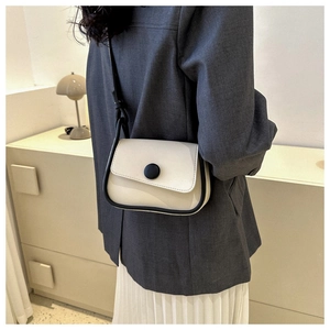 Close-up of a cream crossbody saddle bag with black trim worn with a grey blazer