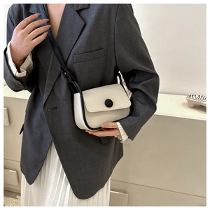 Detail of a minimalist cream crossbody bag with black trim and round button closure