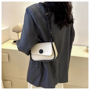 Detail of a vintage-style cream crossbody bag with black trim and a large round button