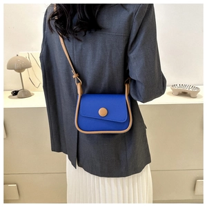 Blue crossbody bag with brown leather trim shown on model in a minimalist home setting