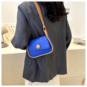 Detail of blue and brown saddle bag worn with a grey blazer and pleated skirt
