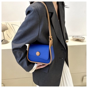 Detail view of a minimalist blue saddle bag with brown leather trim on a model waist