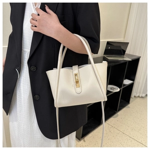 Chique beige trapezium handtas met gouden draaislot gedragen door model op kantoor