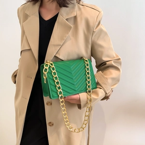 Elegant green quilted chain crossbody bag with V-shaped stitching on beige coat background