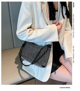 Detail of black rhinestone shoulder bag with silver chain strap on a white blazer