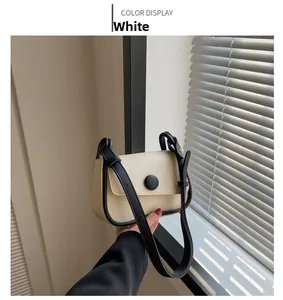 Detail of minimalist cream crossbody bag with black trim and circular buckle ornament
