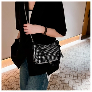 Detail of a sparkling black rhinestone shoulder bag with silver chain worn by a model
