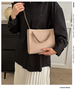Detail of apricot crocodile-patterned bag with gold chain strap on stylish model