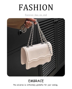 Detail of a creamy white crossbody bag featuring a wavy edge and silver chain strap