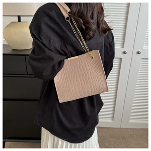 Detail of beige crocodile pattern felt tote bag with metal chain strap on model shoulder