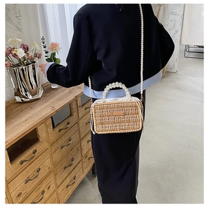 Detail of hand-woven straw bag with elegant pearl top handle and matching crossbody strap