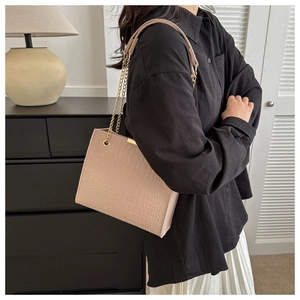 Detail of beige crocodile embossed tote bag with gold chain strap worn over shoulder