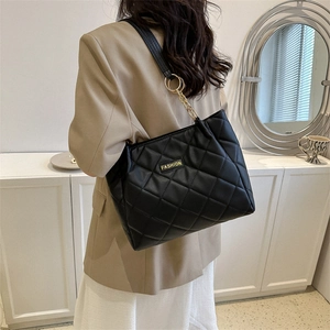 Chic black quilted tote bag with gold chain strap worn by model in minimalist setting