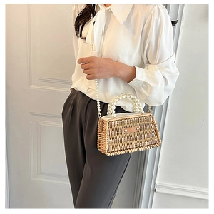 Detail of woven straw handbag featuring large pearl handle and long pearl crossbody chain